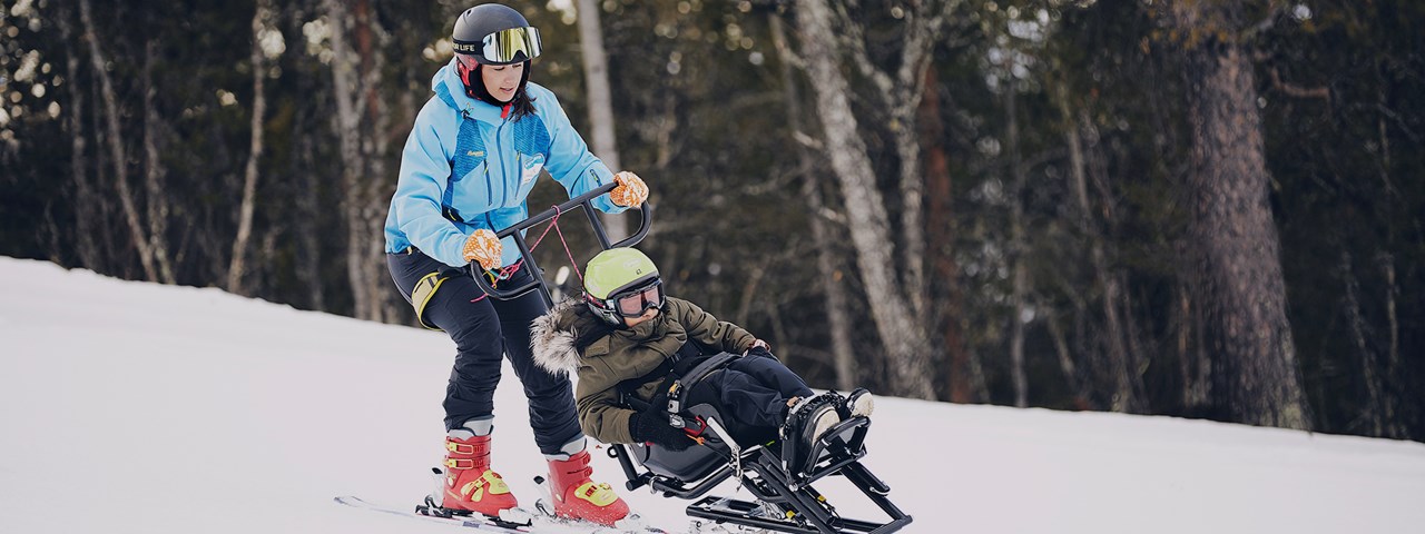 Jente i sit- ski ledsages ned bakken av instruktør. Foto: Christine Stokkebryn